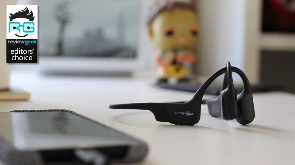 The Aftershokz Aeropex Mini on a desk with a phone in the foreground and Leatherface Pop in the background