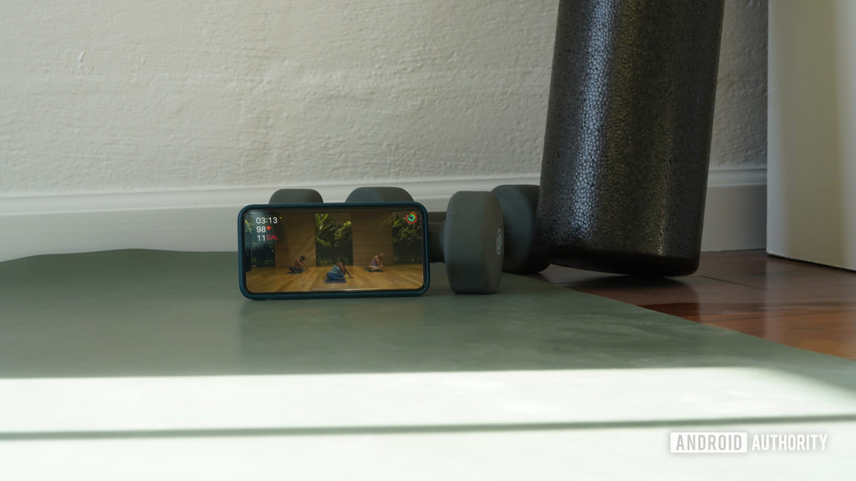 An iPhone at the end of a user's yoga mat plays a yoga workout from Apple Fitness Plus.
