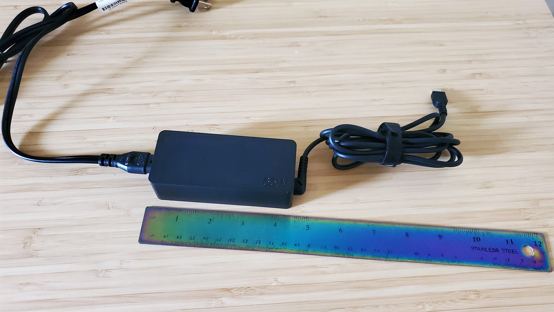 The Lenovo ThinkPad X1 Carbon's 65-watt charger next to a ruler on a desk.