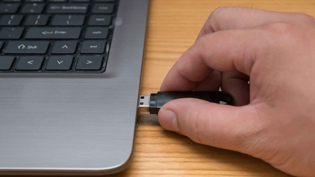 Person's hand plugging a USB drive into a computer.