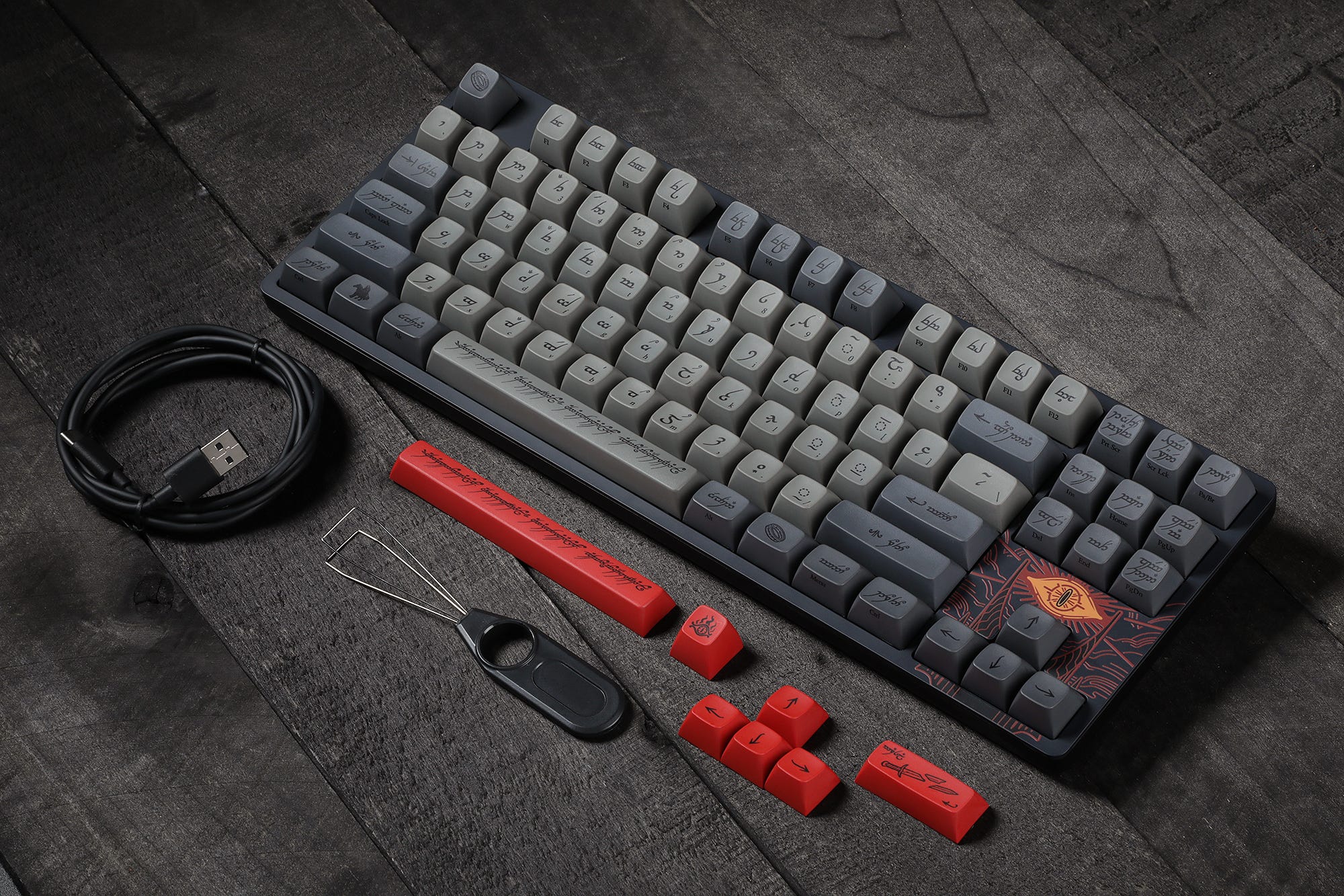 The Drop LOTR Black Speech mechanical keyboard sitting on a table with alternate red and gray keycaps, plus key removal tools.