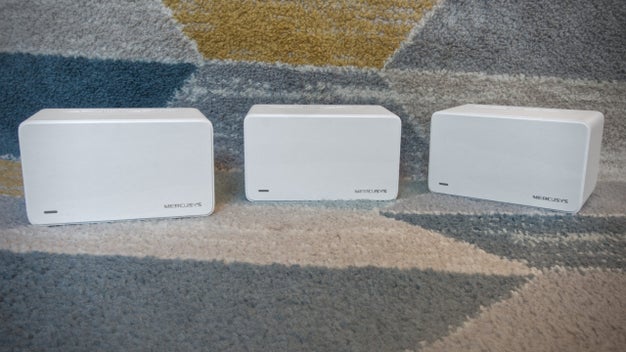 Three white mesh network devices on carpet.