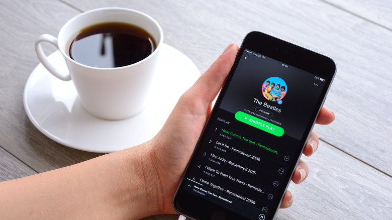 person holding phone with Spotify with coffee