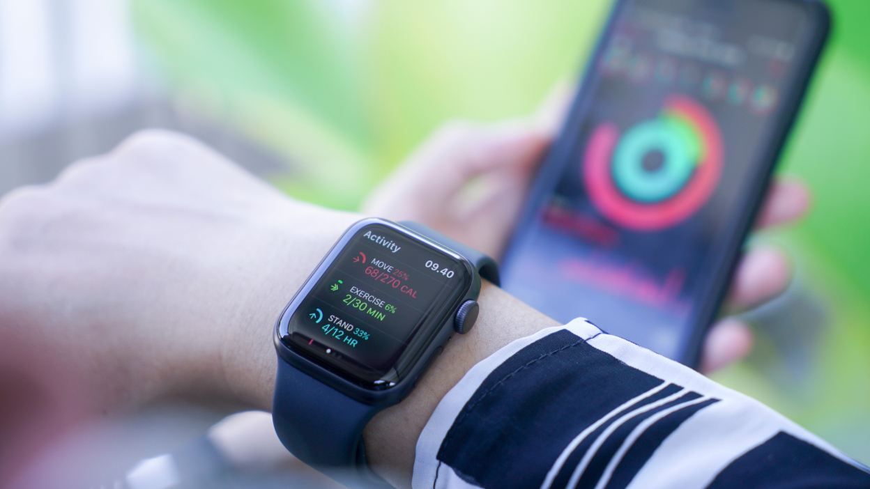 Someone checking fitness activity on their Apple Watch while holding an iPhone with the workout data app open