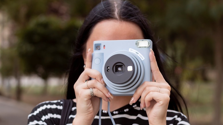 A person holding a newer Polaroid camera in front of their face